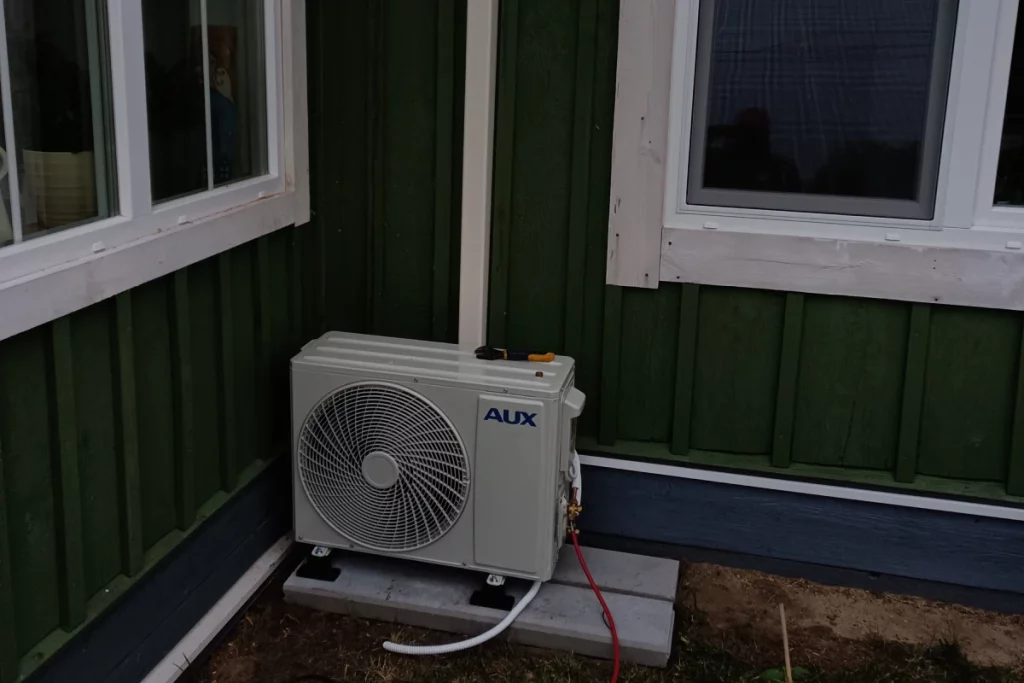 Klimatyzacja Zwierzyniec umieszczona na specjalnym fundamencie obok zielonego, drewnianego domu