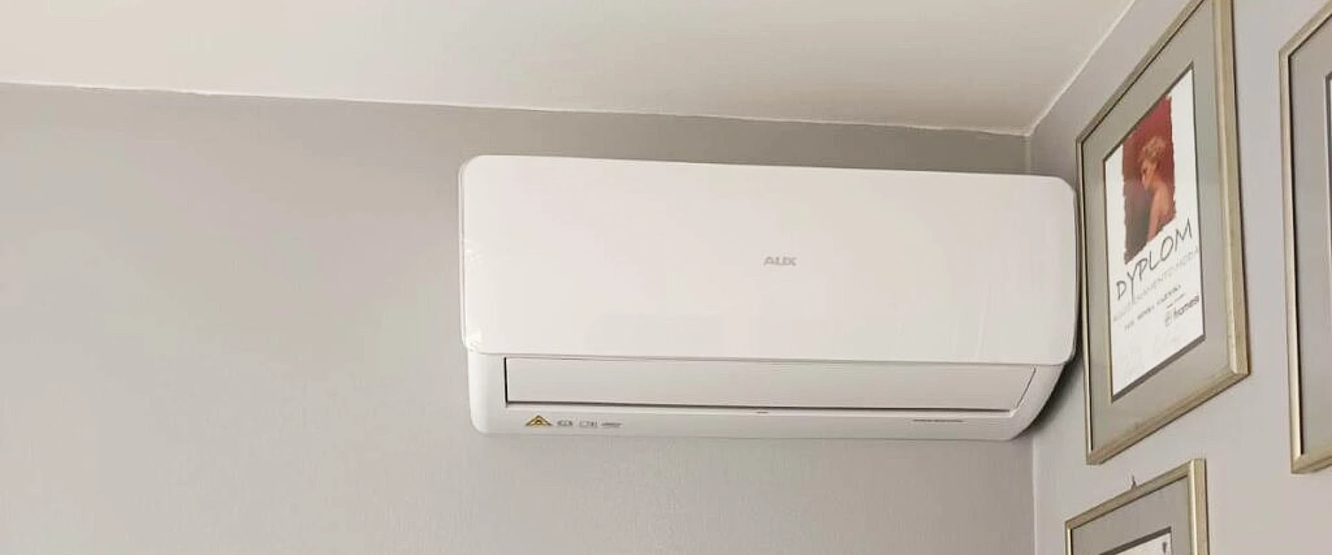 Klimatyzator aux halo zamontowany w salonie fryzjerskim na ścianie obok dyplomów fryzjerskich właściciela